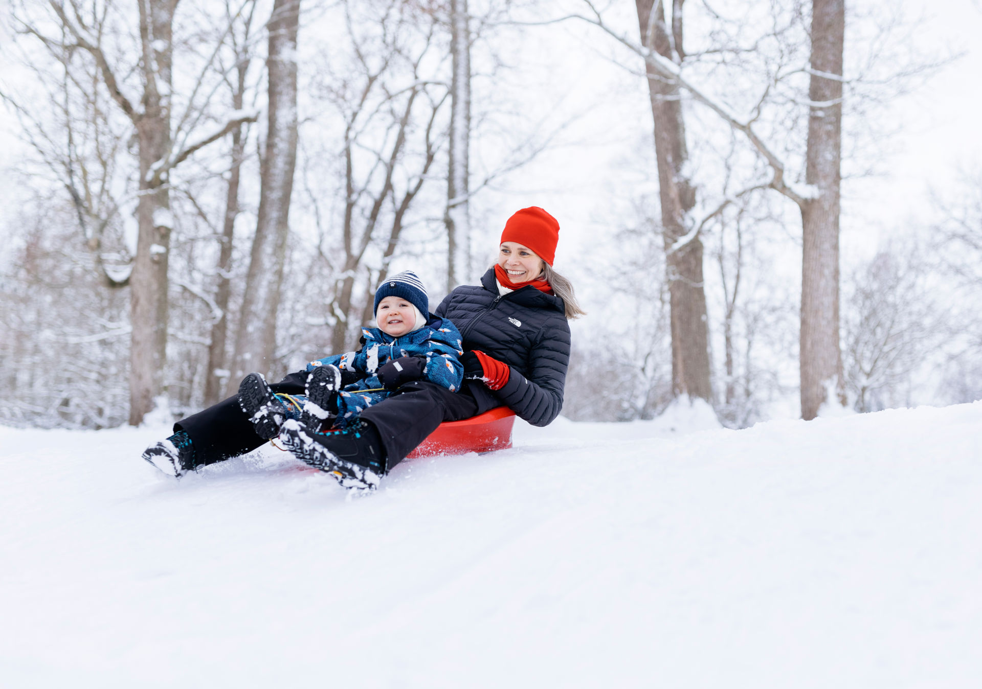 An adult and a child a sliding down a hill on a sled.