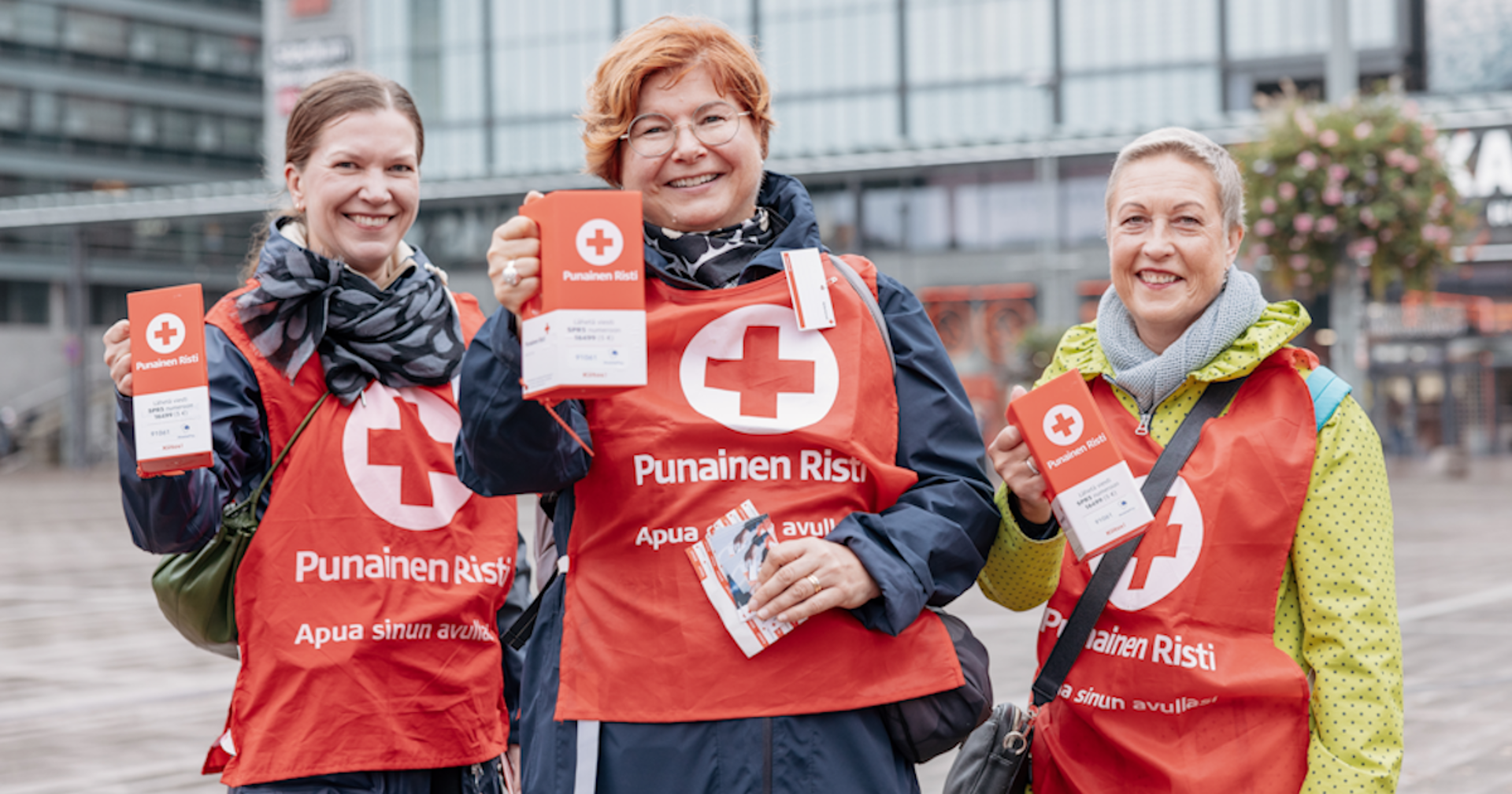 Three people wearing collection vests and holding collection boxes are smiling at the camera.
