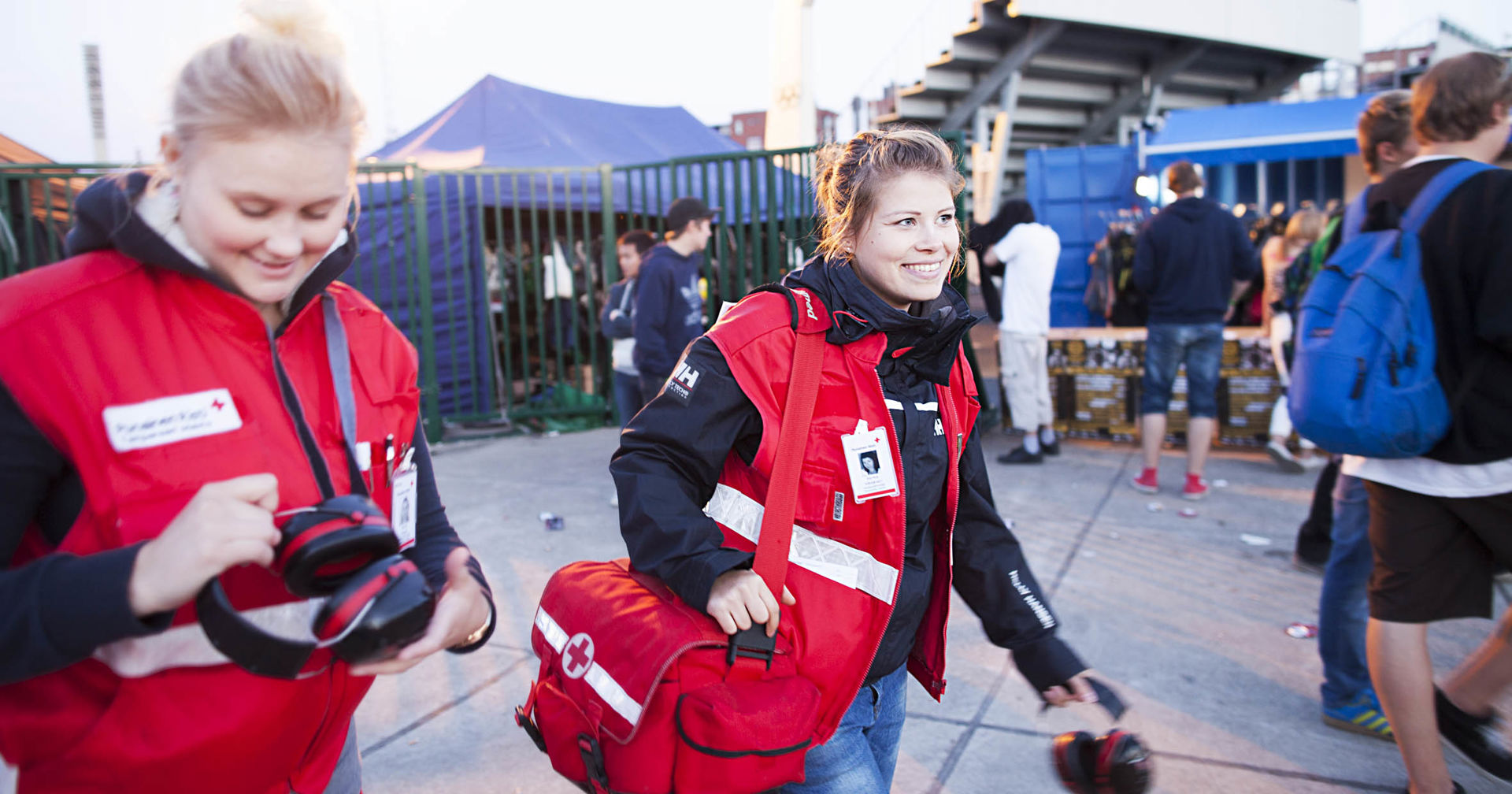 Two people dressed in Red Cross vests are walking outside.