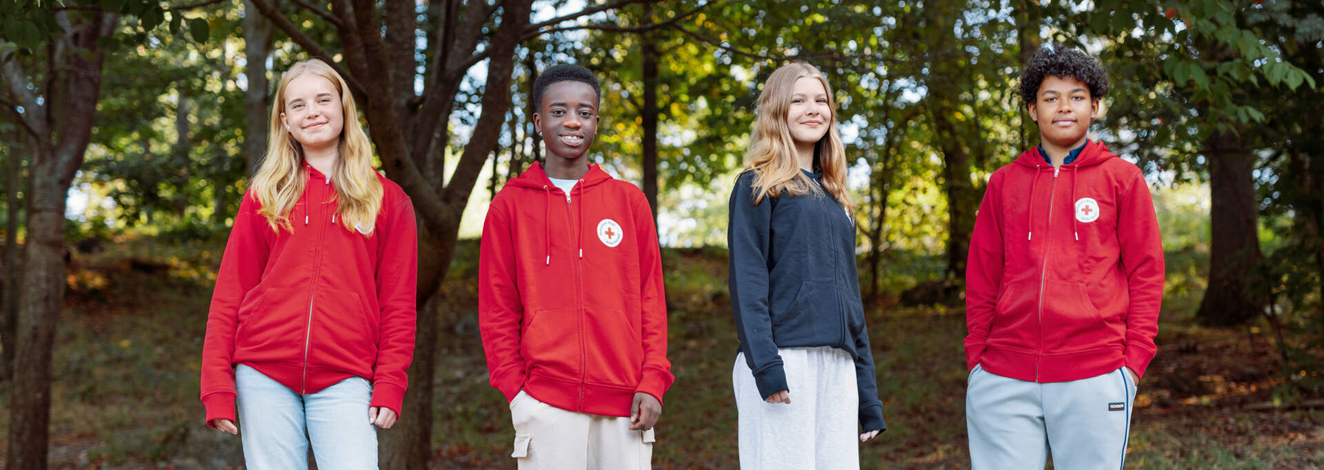 Four young Red Cross volunteers are standing outside. Three of them are wearing a Red Cross red hoodie.