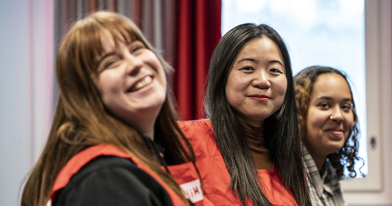 Three young people are sitting and smiling at the camera wearing volunteer vests.