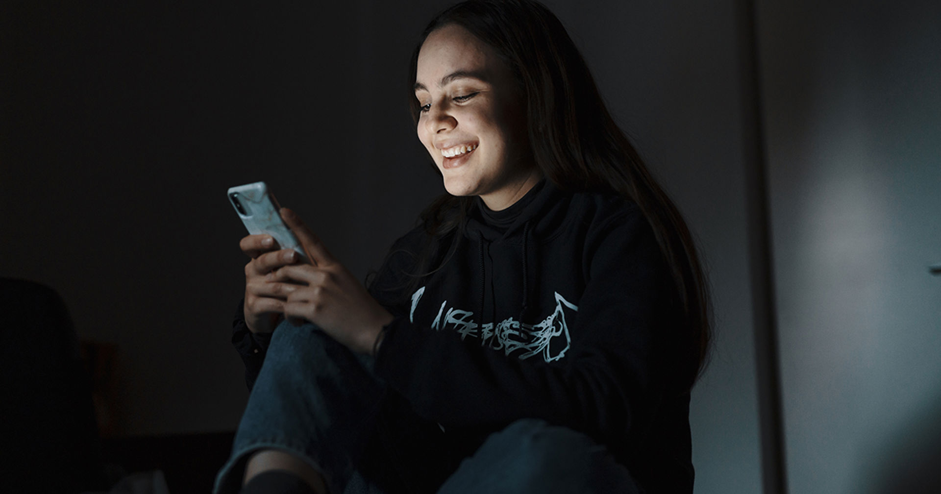 A young person looks at their phone, smiling.