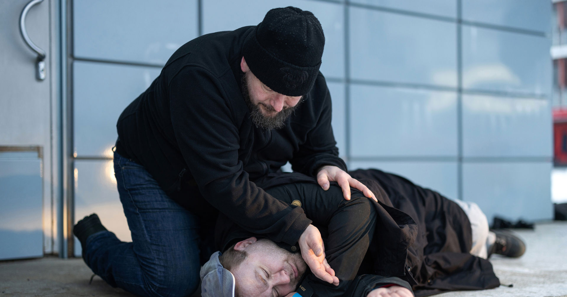 A person is lying on the ground, and another is checking with their hand to see if they are breathing.