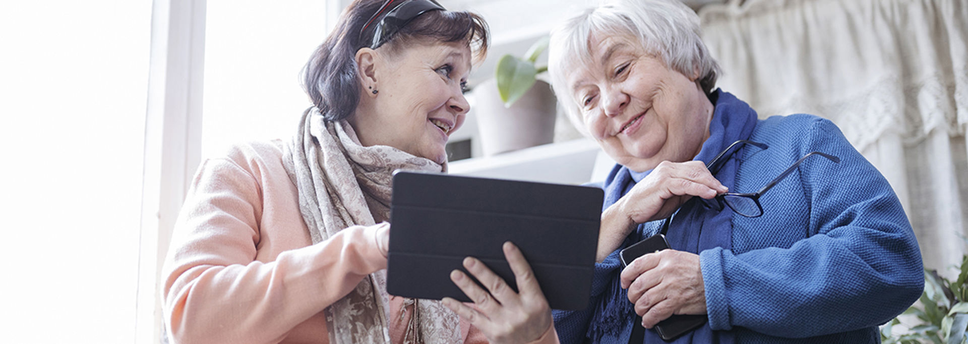 Two people have their hands on a tablet and are smiling at each other.