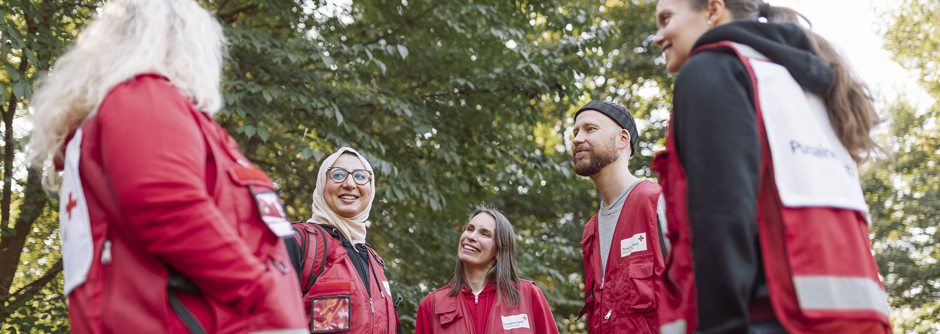 Red Cross volunteers in red vests talking outdoors in a park-like setting.