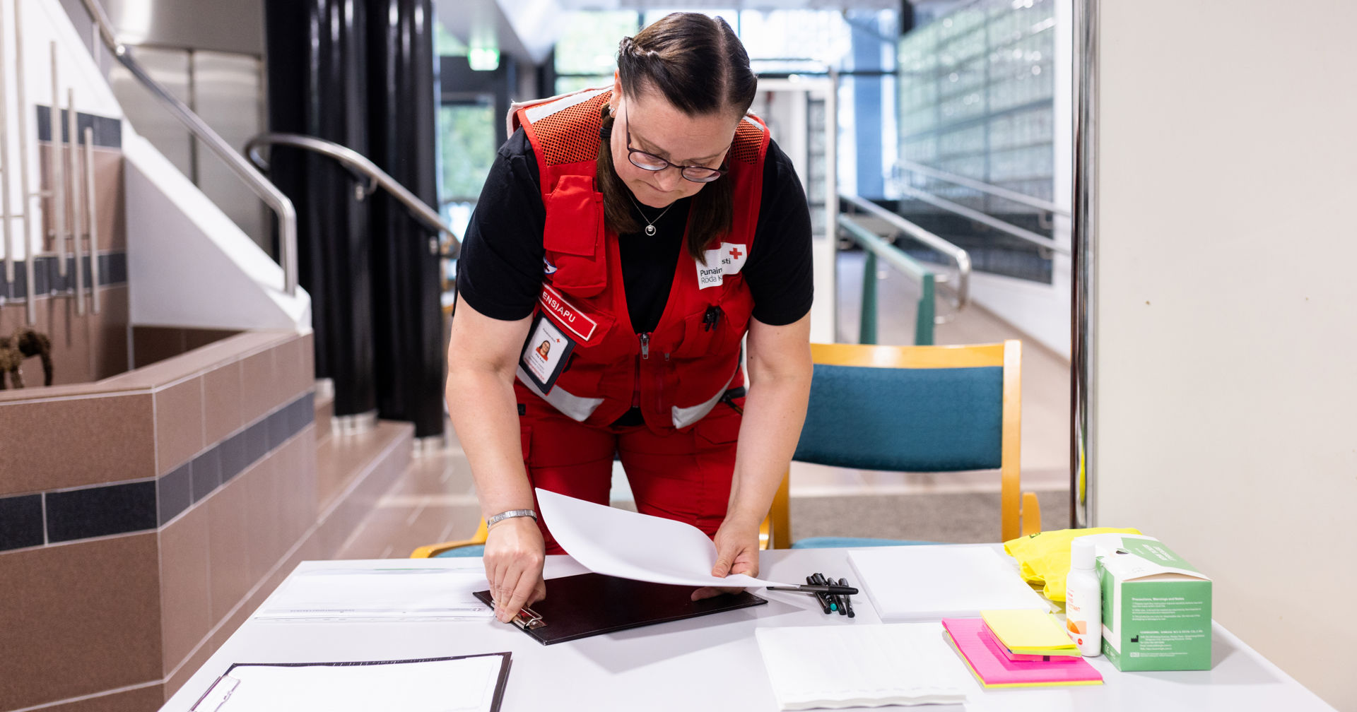 A red cross volunteer is arranging papers that are on a table.