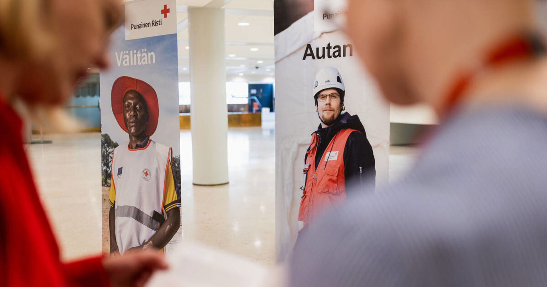 Red Cross roll-ups that read 'I help and I care' in the lobby. Two people reading a brochure in the foreground.