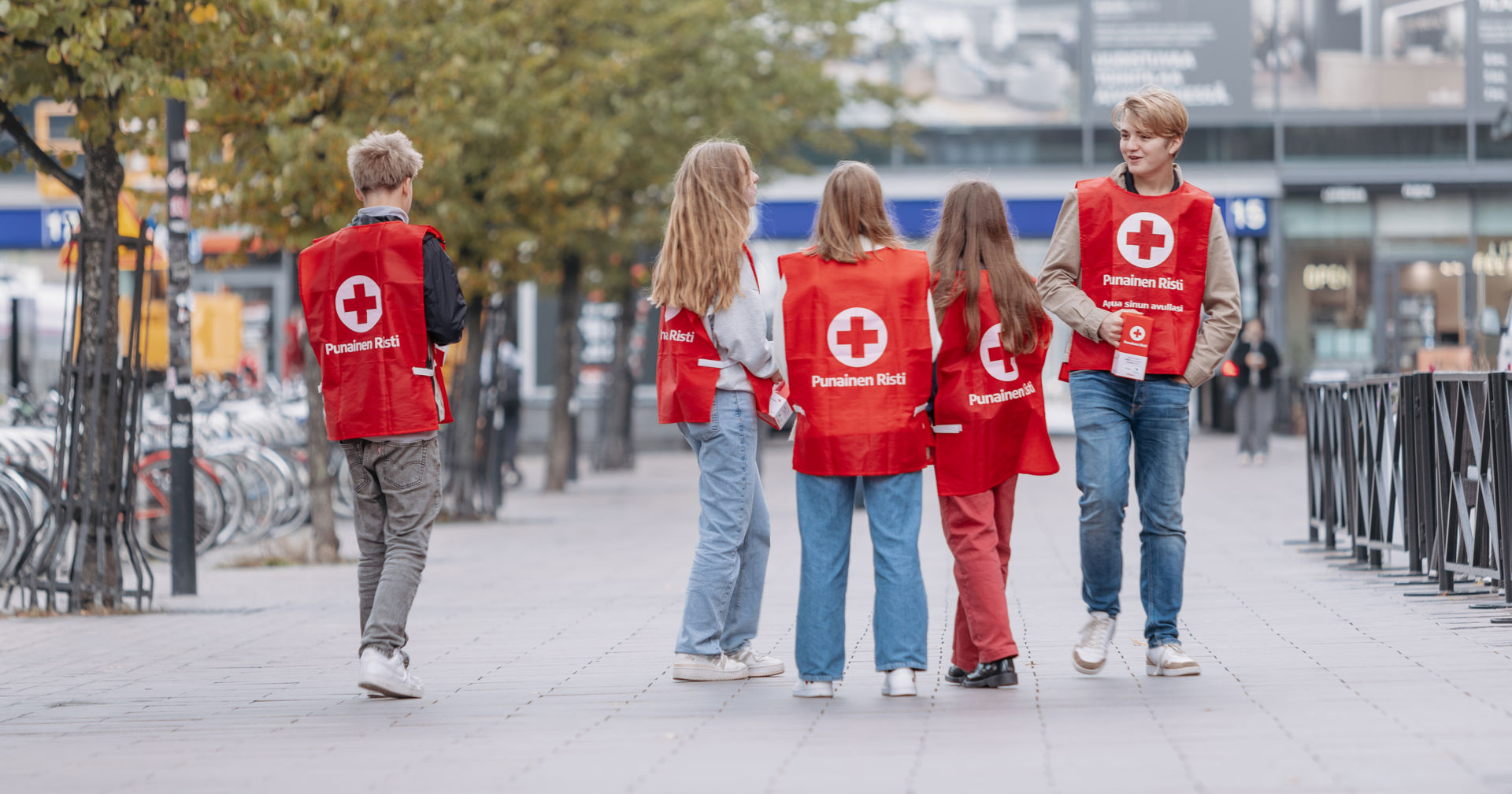 Five young people in a city setting, wearing Red Cross vests and holding Hunger Day collection boxes.