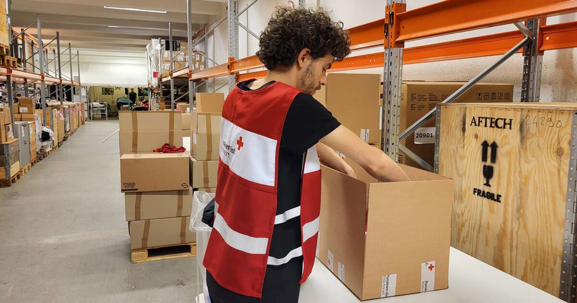 A volunteer with their back to the camera, wearing a volunteer vest that says Red Cross.