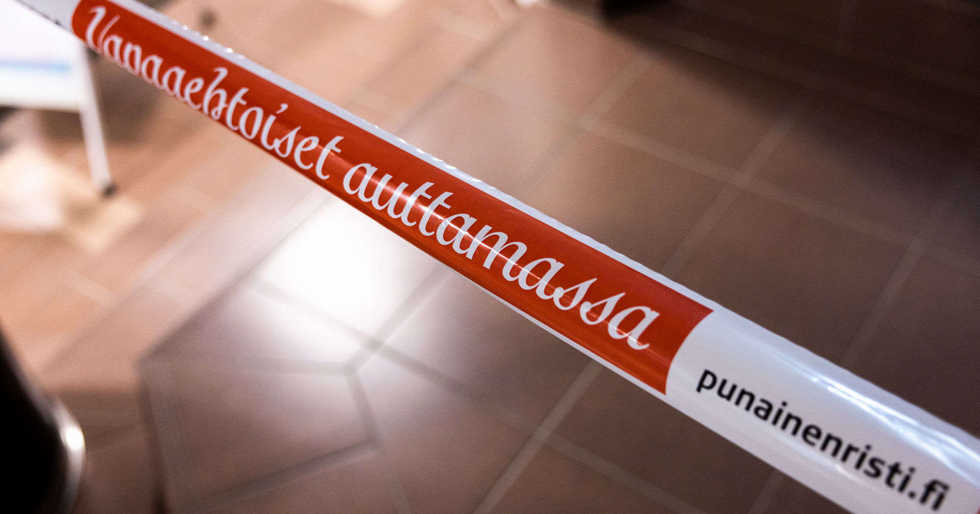 A plastic ribbon reading: Volunteers helping, PunainenRisti.fi