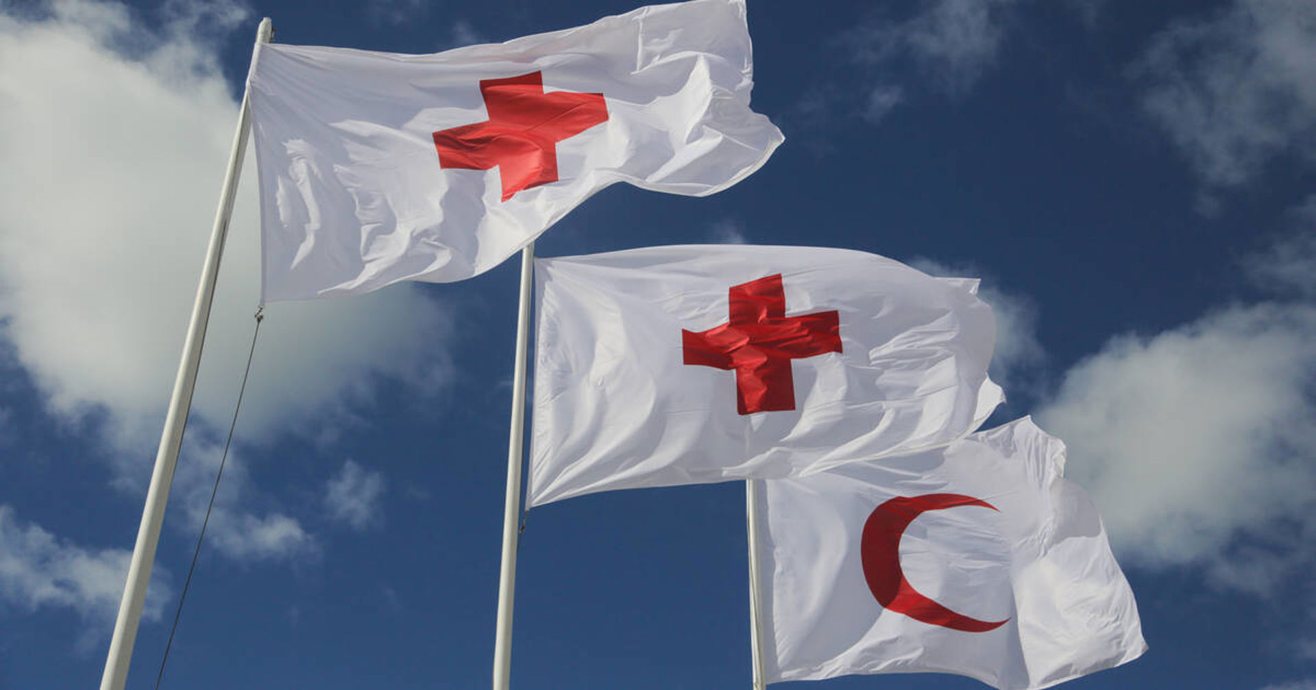 Two flags on flagpoles. One flag bears the Red Cross symbol, the other the Red Crescent.