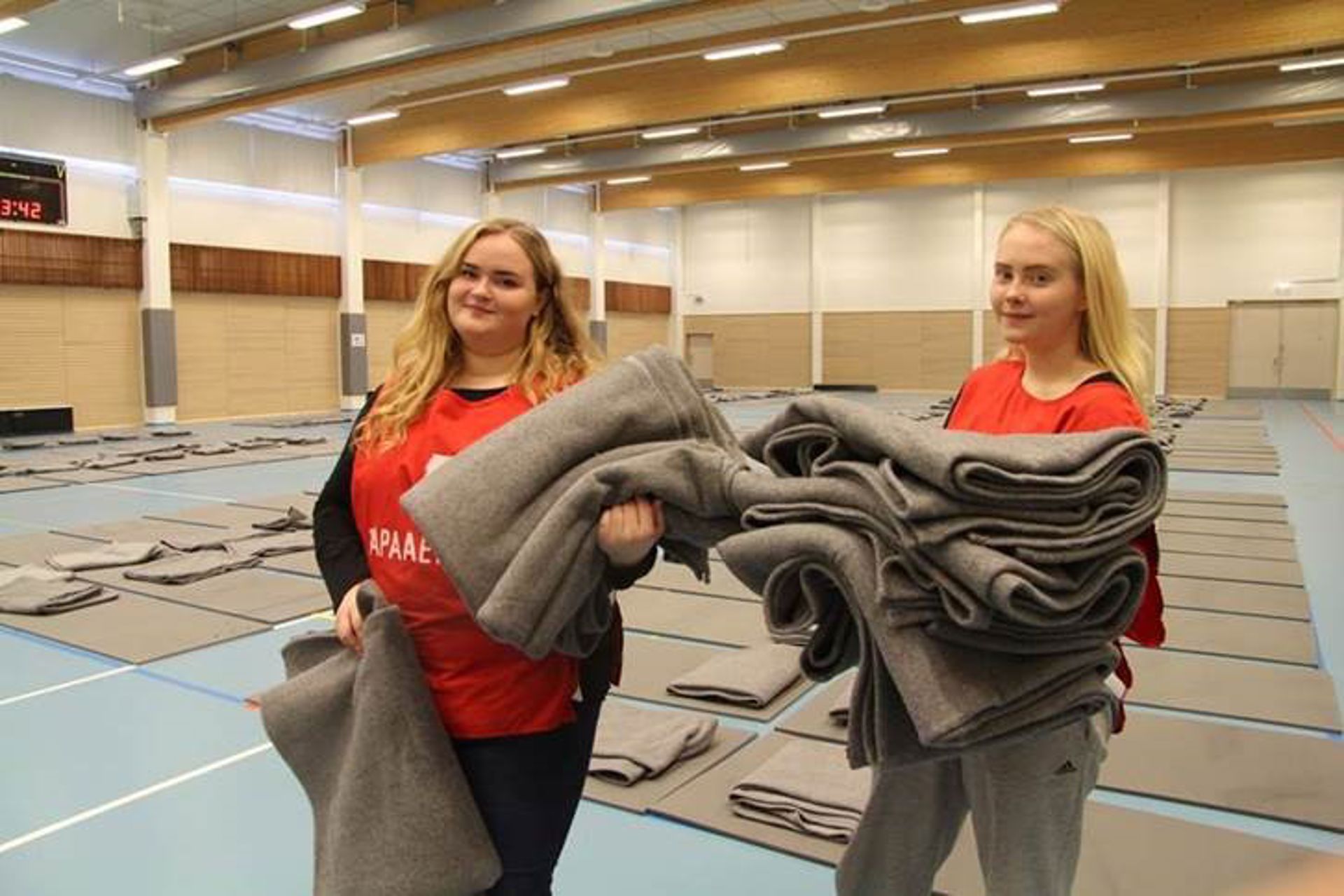 Two Finnish Red Cross volunteers holding blankets in a sports hall.