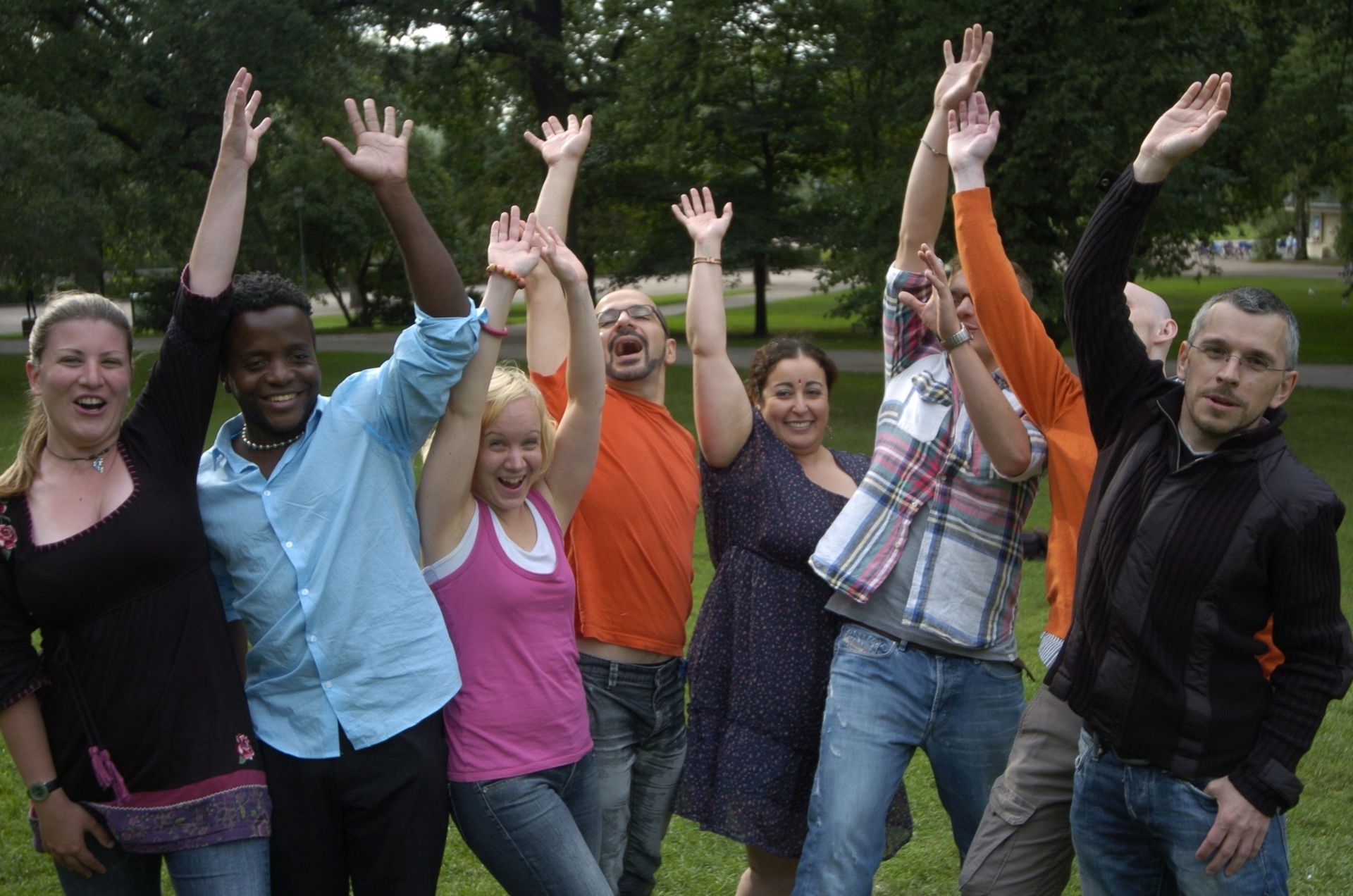 A group of people standing in a park with their hands in the air, smiling.