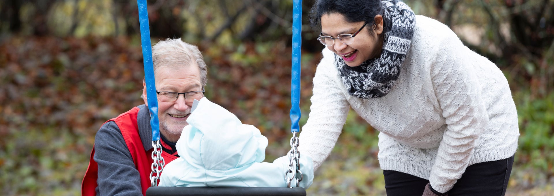 A Red Cross volunteer and a person pushing a child on a swing.