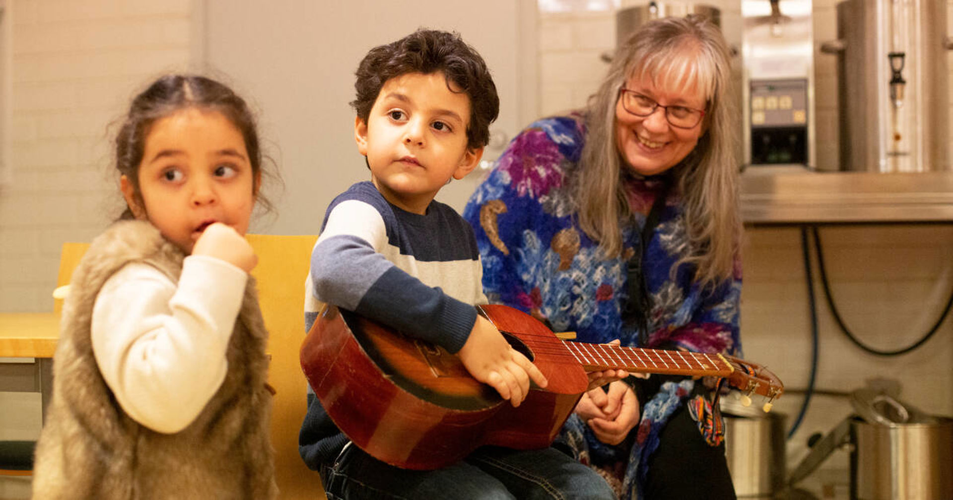 Two children and an adult looking at a guitar.