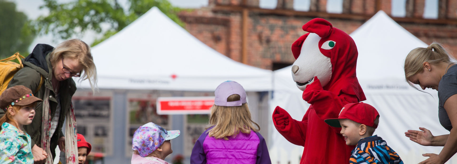 Children dancing with Reddie the Dog at an outdoor event.