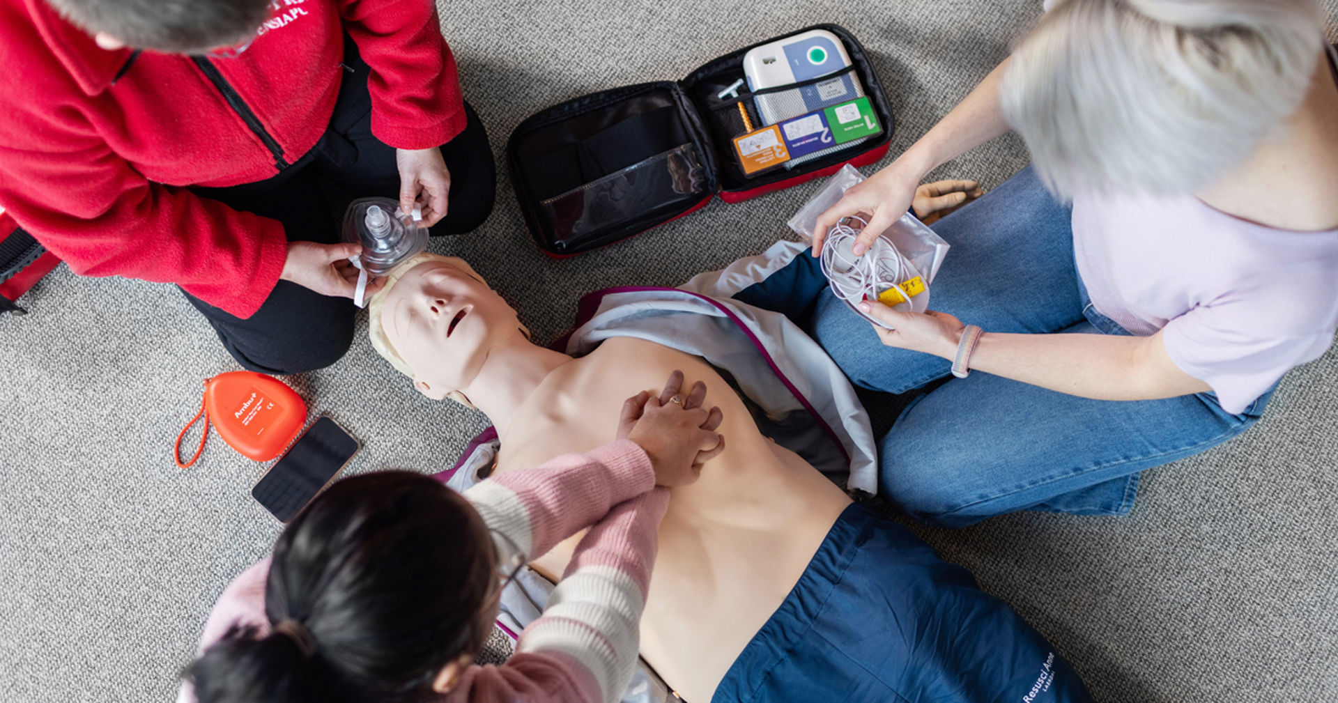 Three people around a CPR manikin.