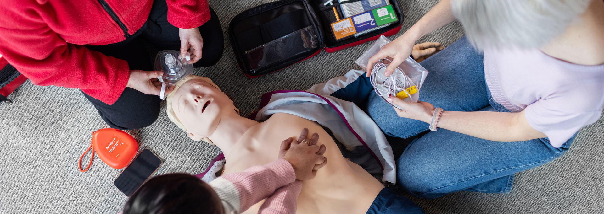 Three people are practicing first aid with a CPR mannequin.