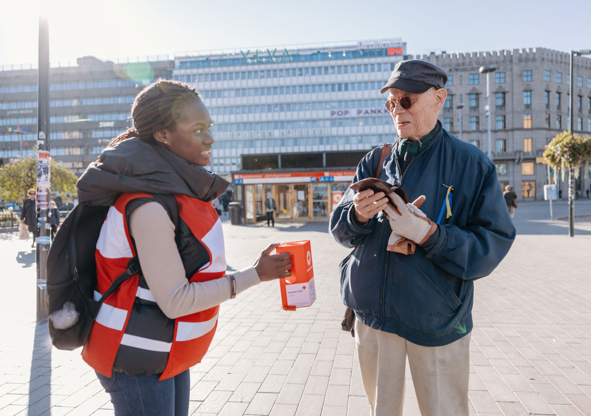 A smiling person puts money into a Red Cross volunteer's collection box.