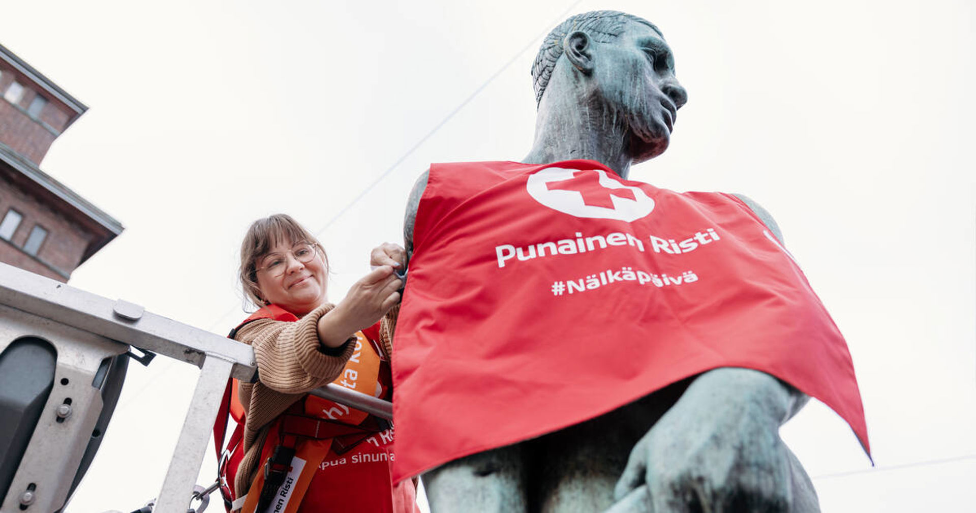 A person is putting a Hunger Day vest on a statue.