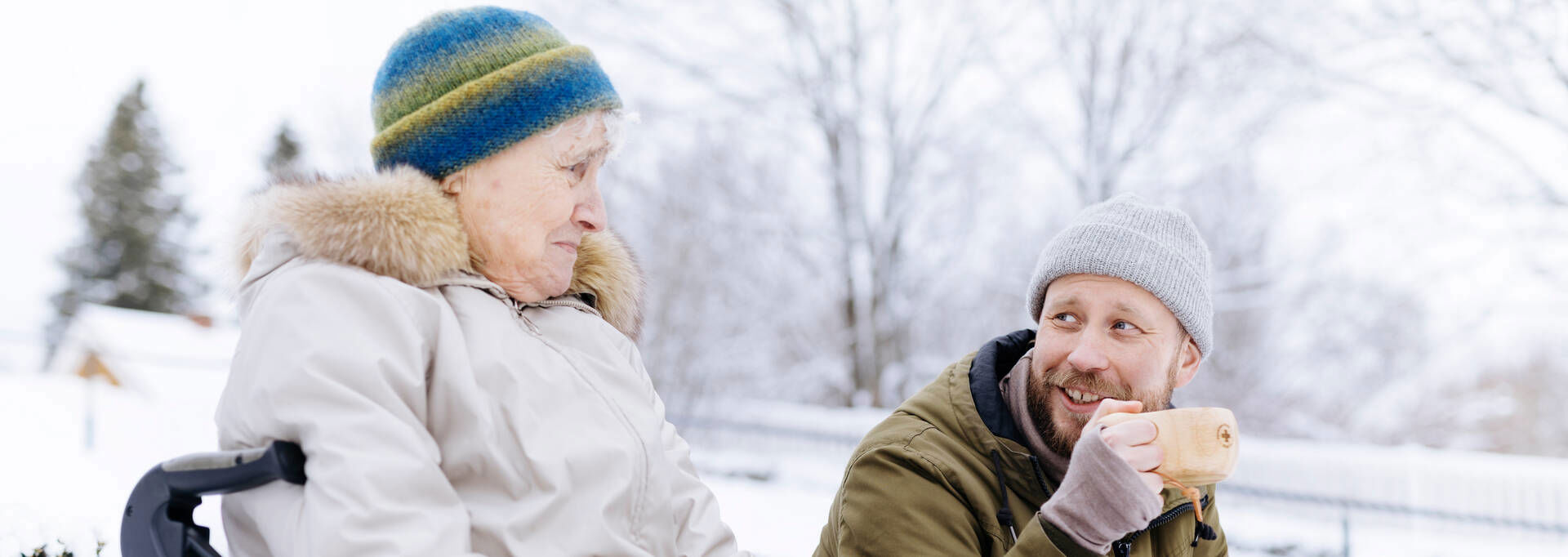 Two people chat and hold steaming cups outside in a winter scenery.