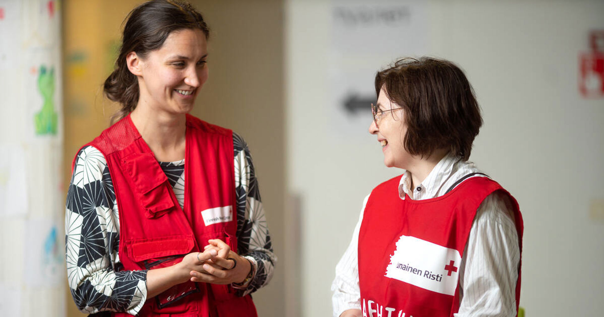 Two Finnish Red Cross volunteers looking at each other smiling.