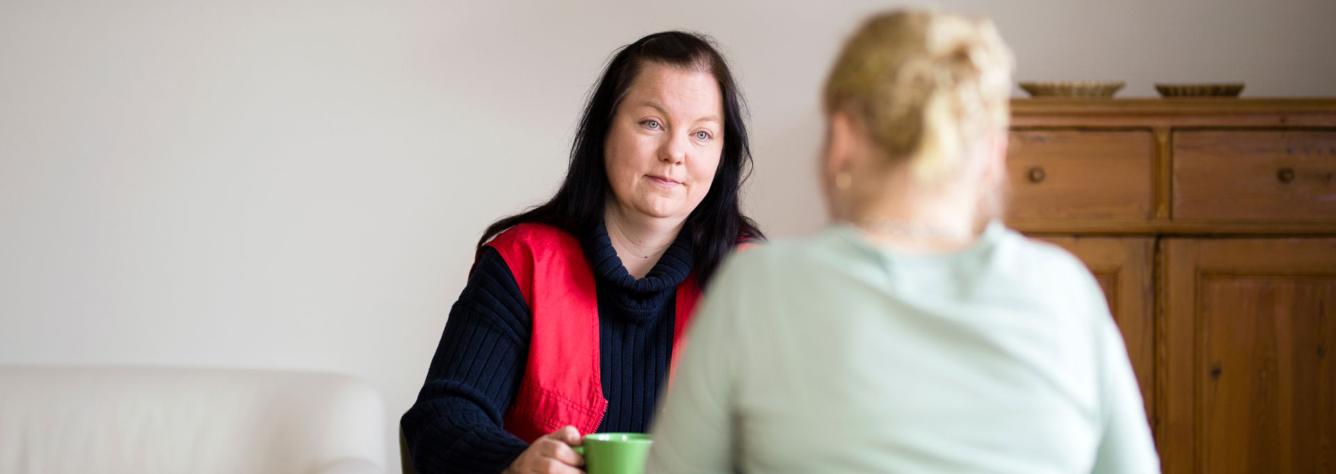 A volunteer and a person sitting at a table across each other. The volunteer is smiling at the person.
